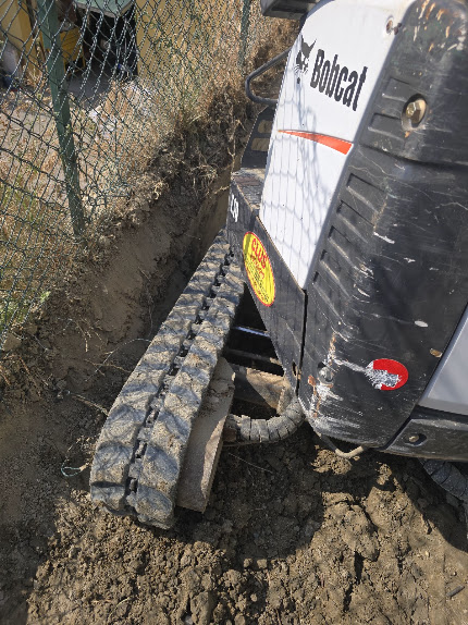 Bobcat Clus Escavazioni impegnato in uno scavo vicino a una recinzione